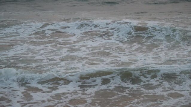 Slow motion closeup shot of sea wave crashing on the shore of Baga beach at Goa in India. Frothy sea wave crashes at the shore of the beach. Sea wave crashing at the sea shore. Summer beach background
