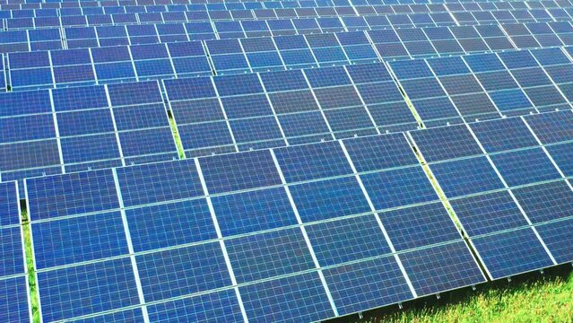 Long rows of sun panels built on grass field at electrical station in rural area on sunny day. Photovoltaic solar cells generate green energy
