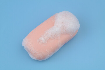 Fototapeta premium Pink soap with foam bubbles on blue background. 