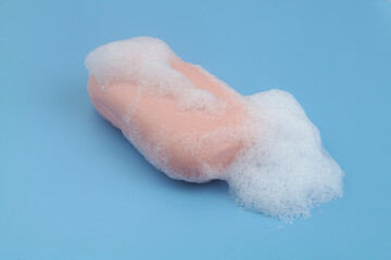 Pink soap bar with foam bubbles on blue background.	