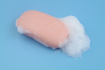 Pink soap bar with white foam bubbles on blue background.	