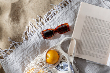 leisure and summer holidays concept - bag of oranges, sunglasses and magazine on blanket on beach sand