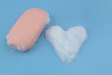 Soap bar and heart shaped foam bubbles  on blue background. Softness and romance concept.