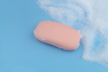 Pink soap bar and white foam on blue background, copy space for text.	