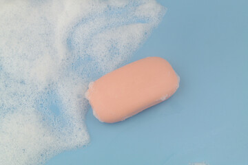 Pink soap and foam on blue background, copy space for text.