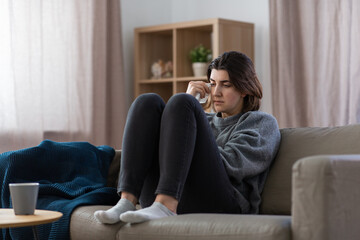 mental health, psychological problem and depression concept - sad crying woman sitting on sofa at home