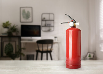 Fire extinguisher on white wooden table in office. Space for text