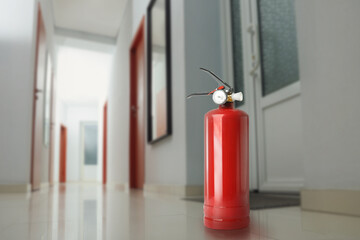 Fire extinguisher on floor in office corridor. Space for text