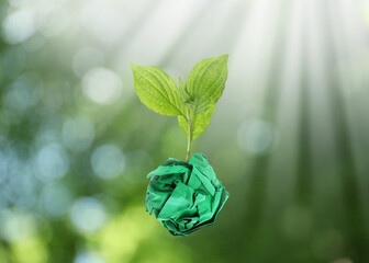 Crumpled sheet of paper on twig with green leaves on blurred background, bokeh effect. Recycling concept