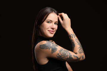 Beautiful woman with tattoos on arm against black background