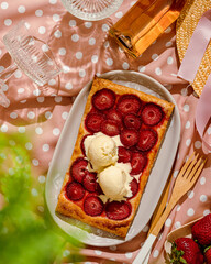delicious strawberry quick and simple tart pie with vanilla ice cream on the pink dottet tablecloth for picnic. summer girls brunch party with strawberry pie and champagne. top view sunny light.
