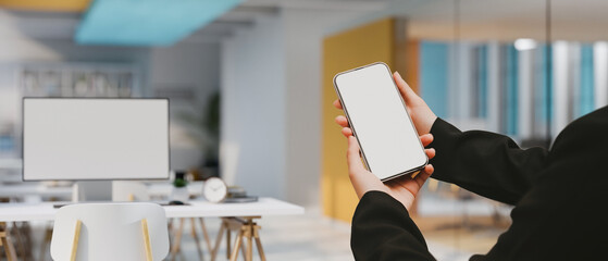 Modern office building workplace interior with a businesswoman's hands holding a smartphone mockup