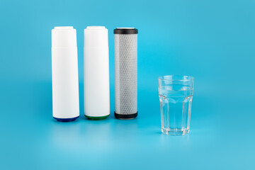 set three of cartridges for water filter with clear glass of water isolated on blue background.  Concept of water treatment technology. filter cartridges to domestic water treatment systems