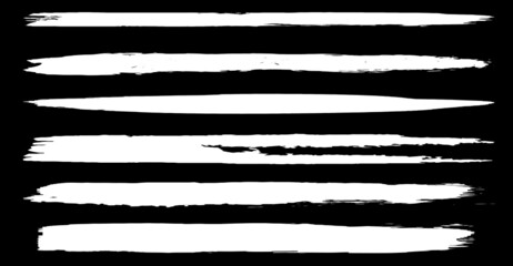 A set of vector brushes in grunge style. White paint strokes with a dry brush on a black background