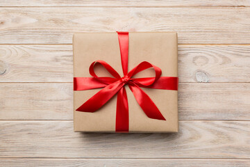 Holiday gift box wrapped in craft paper with colored bow on table background. Top view, flat lay, copy space