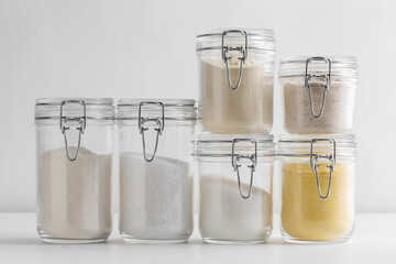 food, culinary and storage concept - jars with different kinds of flour sugar and salt on white...