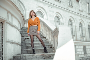 Obraz premium A middle-aged woman looks like a good blonde with curly beautiful hair and makeup on the background of the building. She is wearing a yellow sweater.