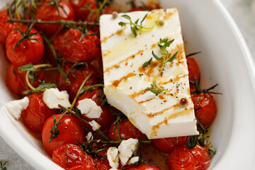 Baked cherry tomatoes and Feta cheese with oil, garlic and thyme in white dish. Close up. Fresh Diet dinner idea. Baked feta pasta.