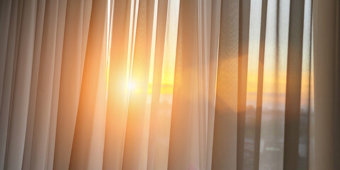 Bright sunlight shines through transparent silk curtain hanging at room. Ray of sun illuminate apartment at sunset or sunrise.