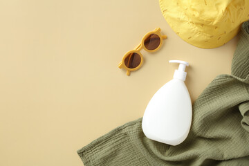 Baby suntan lotion bottle, kids sunglasses, panama hat, towel on beige background.