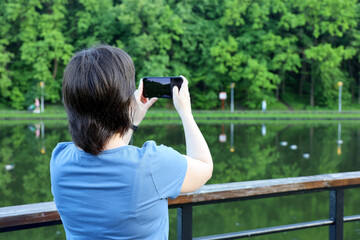 Woman photograph on smartphone camera the lake in summer park. Travel and leisure on a nature