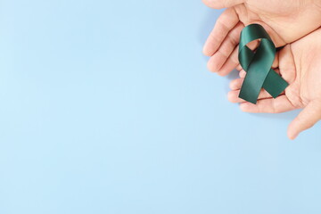 Top view of hand holding color teal awareness ribbon. PCOS, sexual assault and ovarian cancer care and prevention concept.