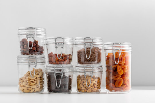 food, healthy eating and diet concept - jars with dried fruits and seeds nuts on white background