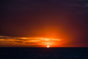 Sun with rays at sunset in the open ocean.
