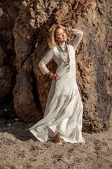Middle aged woman looks good with blond hair, boho style in white long dress on the beach decorations on her neck and arms.