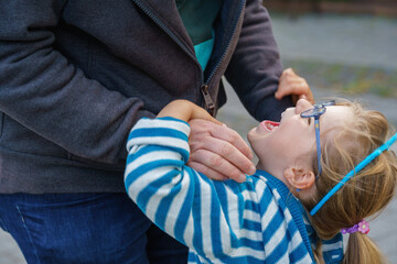 Happy child preschool girl smiles and holds father's hand on the way to school on the first sunny day of class. Dad and daughter on the way to kindergarten, fun together. Child with glasses.