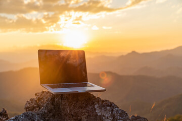 Laptop computer on rock mountain sunset background.