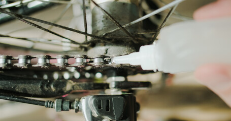 Lubrication of a bicycle chain with oil-lubricant. Close-up, top view. The hand drips from the tube over the links of the chain.