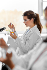 science research, work and people concept - female scientist with chemical or test sample in beaker...