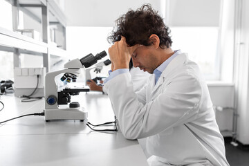 science research, work and people concept - tired male scientist with microscope working in...