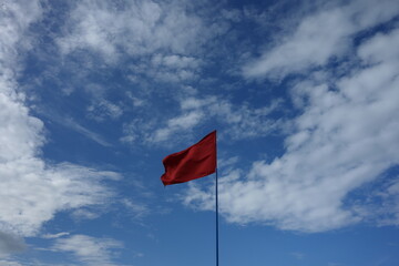 red flag on a blue cloudy sky in summer prohibit swimming