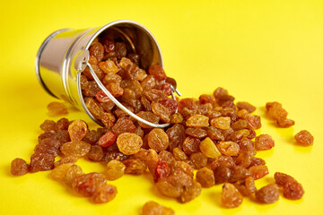 A small bucket filled with raisins on a yellow background.