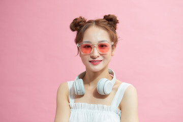 young excited girl wearing glasses and wireless headphones around neck isolated on pink background