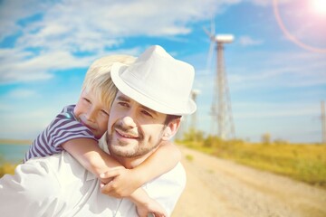 Happy dad carrying child on shoulders checking future project at wind farm site on sunset.