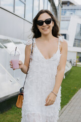 Portrait of a young woman who drinks a refreshing cocktail on a hot summer day. A model in a stylish white dress and sunglasses