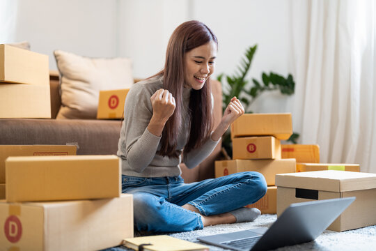 Asian woman working at small business ecommerce with laptop very happy and excited doing winner gesture with arms raised, smiling and screaming for success. celebration concept.
