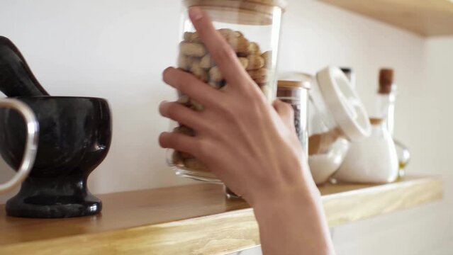 The hostess woman takes a jar of unpeeled peanuts from a shelf in the kitchen, a woman's hand takes a jar of kitchen utensils from a shelf in the kitchen. Preparing a healthy high-calorie breakfast
