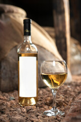 Glass and bottle of white wine in the wine cellar. Bottle with a label-preparation for designers