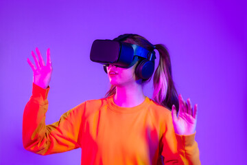 Young asian woman in orange sweatshirt wearing black vr headset watching and hand touching on the purple background. Metaverse concept vr future girl lifestyle.