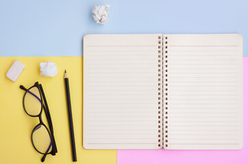 Notebook, Black pencil,Eyeglasses and eraser on pink,yellow and blue background