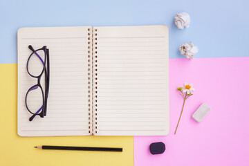 Notebook ,Black pencil,Eyeglasses,Eraser and White Flower on Pink,Yellow and Blue Background