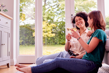 Same Sex Female Couple Or Friends Relaxing At Home Sitting In Lounge Celebrating With Glass Of Wine