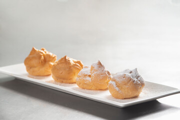 Decorating profiteroles with powdered sugar. Eclairs with icing sugar on black background