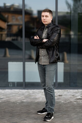 A confident young man in a black jacket and looking at the camera while standing outdoors