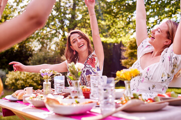 Three Female Friends Sitting Outdoors In Summer Garden At Home Eating Meal Together