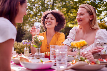 Three Female Friends Sitting Outdoors In Summer Garden At Home Eating Meal Together